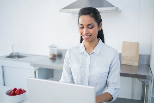 Adorável jovem mulher trabalhando em notebook em pé na cozinha brilhante — Fotografia de Stock