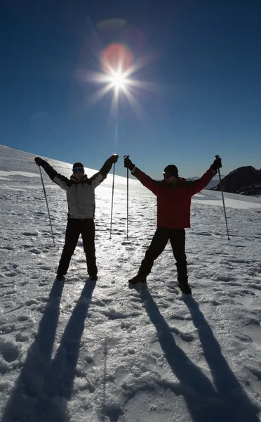 Casal de silhueta que levanta mãos com bastões de esqui em neve — Fotografia de Stock