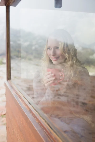 Nachdenkliche, zufriedene Frau mit Kaffeetasse blickt durchs Fenster — Stockfoto