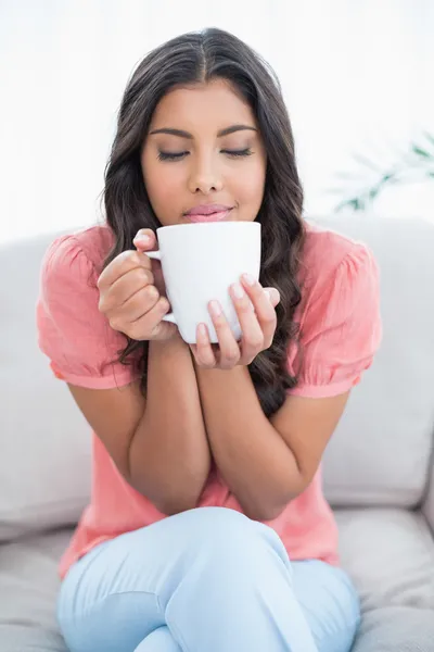 Genießen süße Brünette sitzt auf der Couch hält Becher — Stockfoto