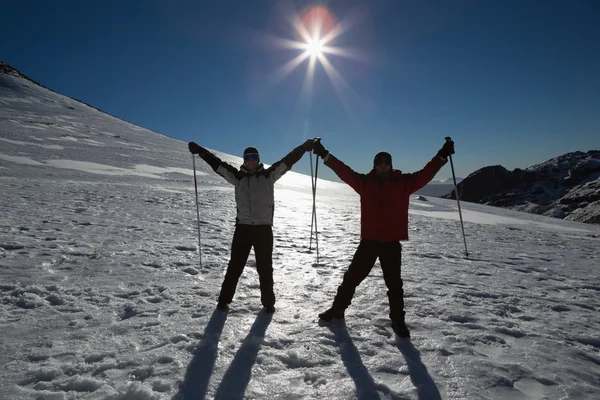 Sylwetka para podnoszenia rąk z kijki narciarskie na śniegu — Zdjęcie stockowe
