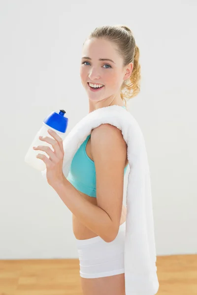 Uśmiechający się szczupła blondynka stoi i trzymając butelkę sportowe — Zdjęcie stockowe