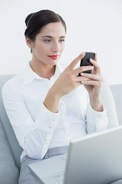 Mujer bien vestida usando teléfono celular y portátil en el sofá — Foto de Stock