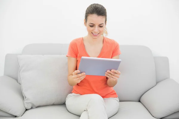Mujer tranquila contenido usando su tableta sentada en el sofá —  Fotos de Stock