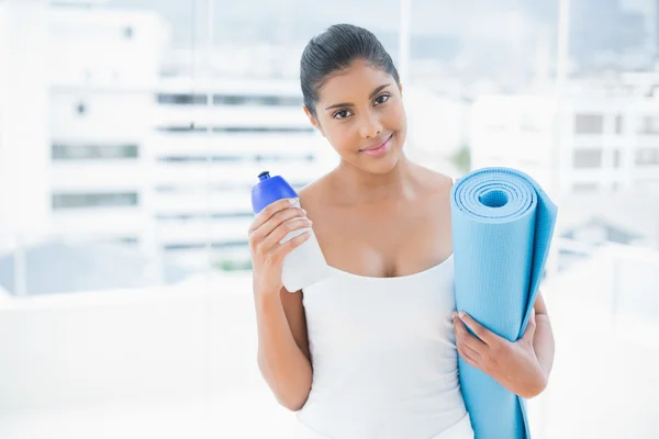 Радостная брюнетка держит спортивную бутылку и коврик для упражнений — стоковое фото