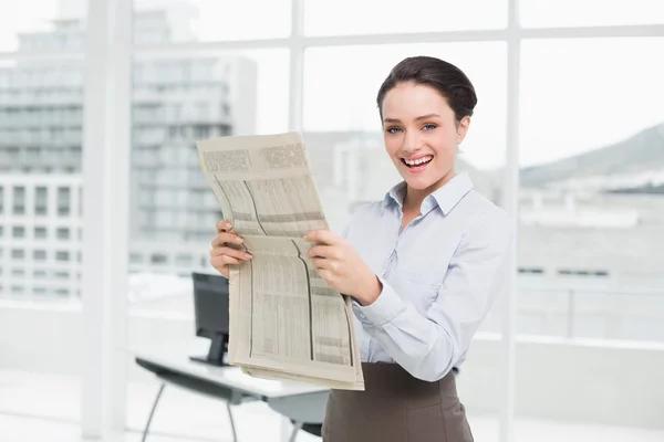 Smiling young businesswoman with newspaper in office — Stock Photo, Image