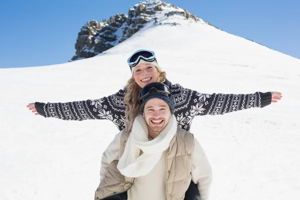 Wan piggybacking mulher alegre contra neve coberta colina — Fotografia de Stock