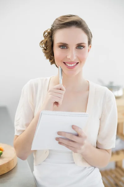 Veselá žena myslet při zápisu nákupní seznam v její kuchyni — Stock fotografie