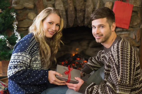 Man gifting woman in front of lit fireplace during Christmas — Stock Photo, Image