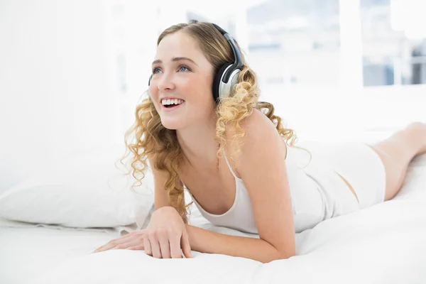 Pretty smiling blonde lying in bed listening to music — Stock Photo, Image