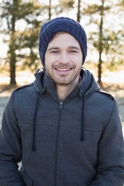 Lächelnder junger Mann in warmer Kleidung im Wald — Stockfoto