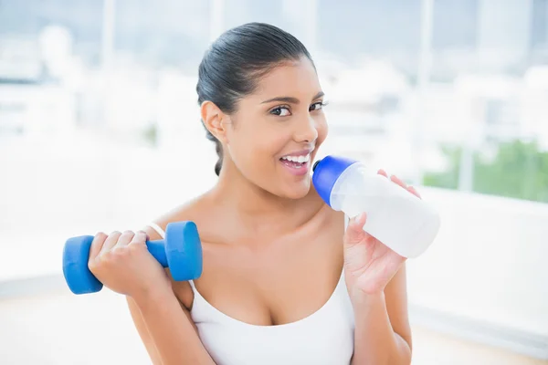 Happy toned brunette holding dumbbells and sports bottle — Stock Photo, Image