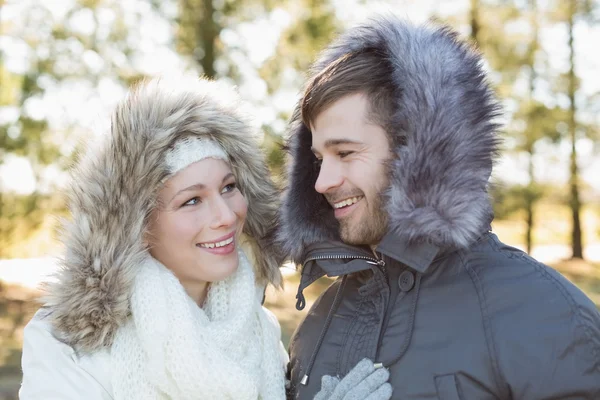 Smiling couple in fur hood jackets in the woods — Stock Photo, Image