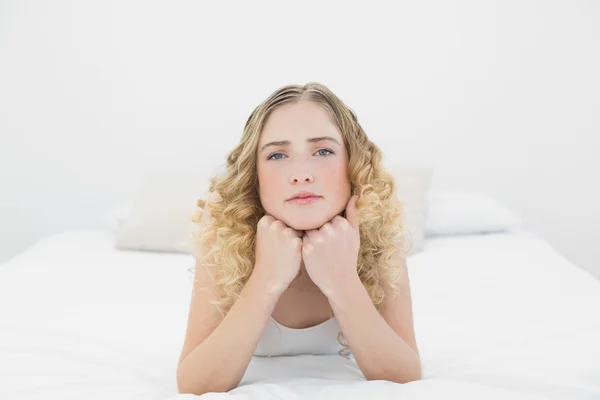Pretty frowning blonde lying on bed looking at camera — Stock Photo, Image