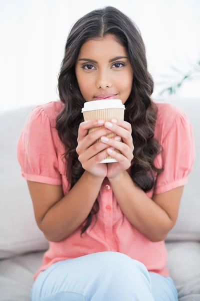 Spokojny, ładny brunetka siedzi na kanapie, trzymając filiżanki jednorazowe — Zdjęcie stockowe