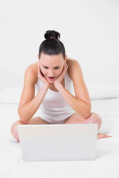 Scioccato donna casuale utilizzando il computer portatile a letto — Foto Stock