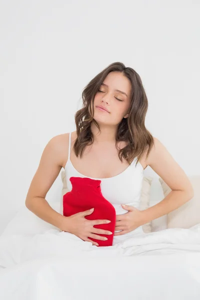 Mujer con botella de agua caliente en el estómago en la cama — Foto de Stock
