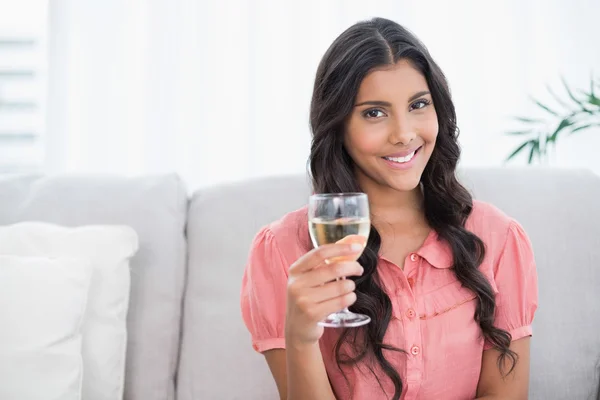 Glad söt brunett sitter på soffan håller vitt vin glas — Stockfoto