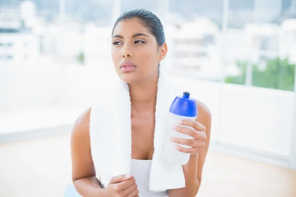 Poważne stonowanych brunetka z ręcznikiem, trzymając butelkę sportowe — Zdjęcie stockowe