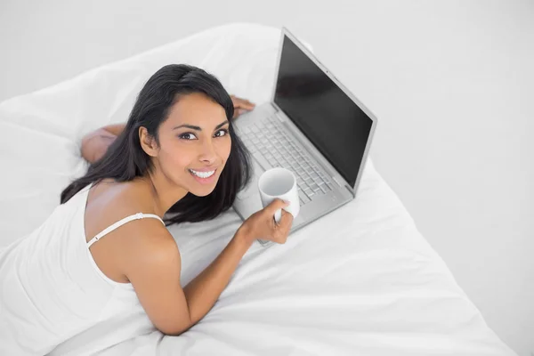 Mujer natural contenta sosteniendo una taza acostada en su cama —  Fotos de Stock