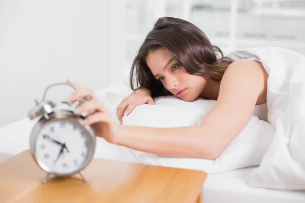 Woman in bed extending hand to alarm clock — Stock Photo, Image