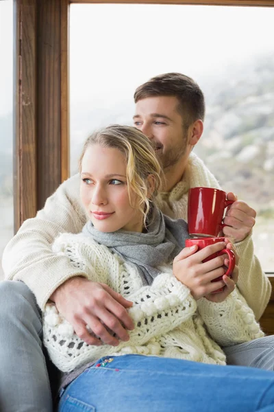 Пара в зимовому одязі з чашками, які виглядають через вікно — стокове фото