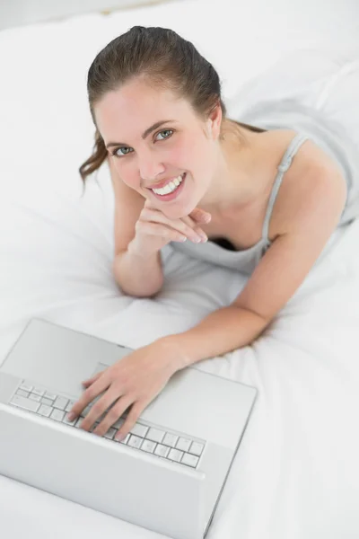 Sonriente mujer casual utilizando el ordenador portátil en la cama — Foto de Stock