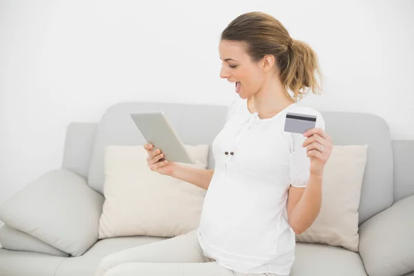 Linda mujer embarazada animando usando su tableta para ir de compras a casa — Foto de Stock