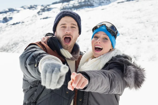 Couple in jackets pointing at the camera on snow covered landsca — Stock Photo, Image