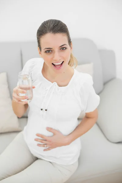 Glücklich schwangere Frau hält ein Glas Wasser und lächelt in die Kamera — Stockfoto