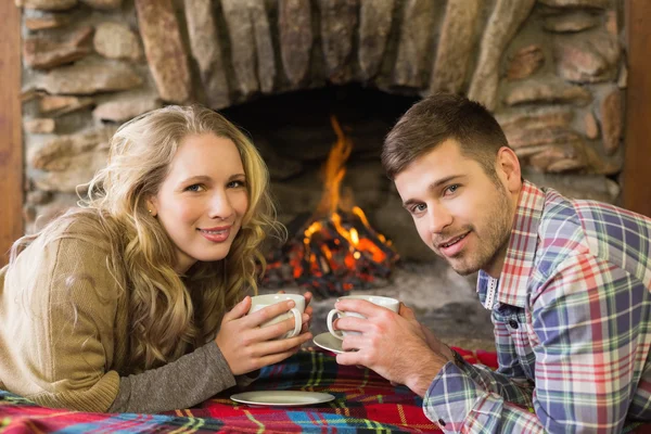 Casal com xícaras de chá na frente da lareira acesa — Fotografia de Stock