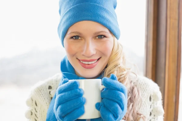 Lachende vrouw met cup in warme kleding tegen venster — Stockfoto