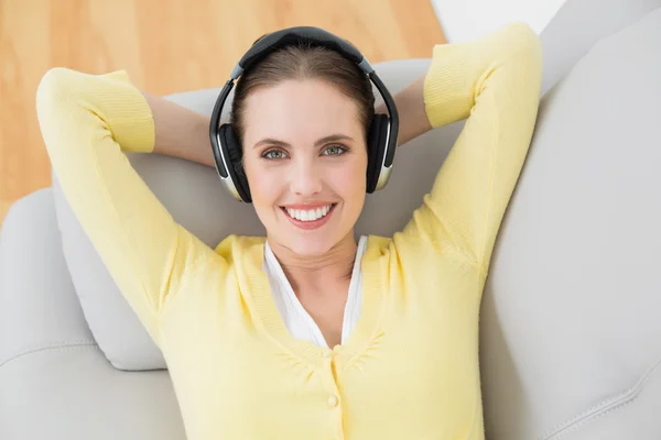 Mujer escuchando música a través de auriculares en el sofá —  Fotos de Stock