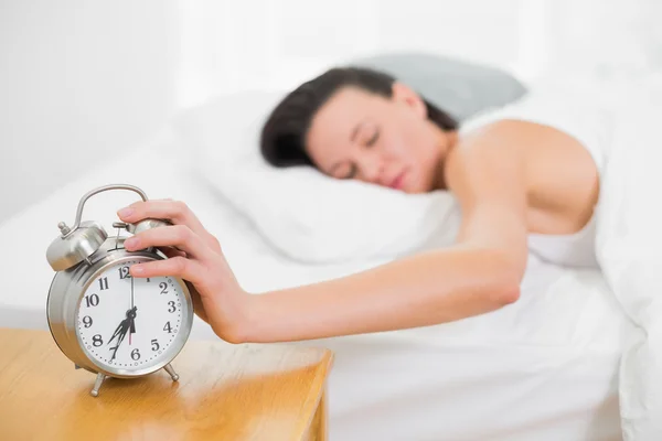 Mujer en la cama extendiendo la mano al despertador en casa —  Fotos de Stock