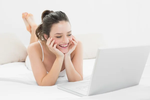 Smiling casual woman looking at laptop in bed — Stock Photo, Image