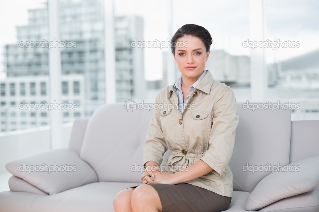 Serious well dressed woman sitting on sofa at home