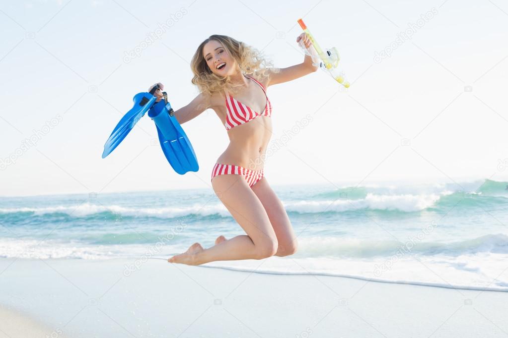 Happy woman jumping while holding flippers and a snorkel
