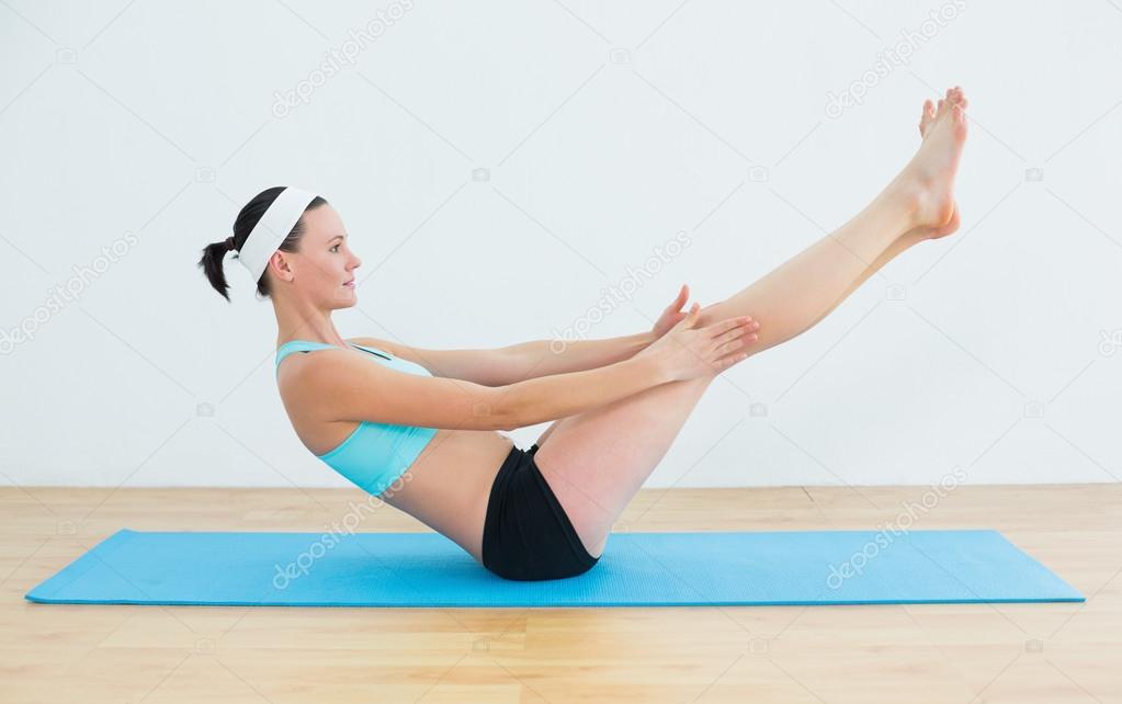 Fit woman doing the boat pose on yoga mat
