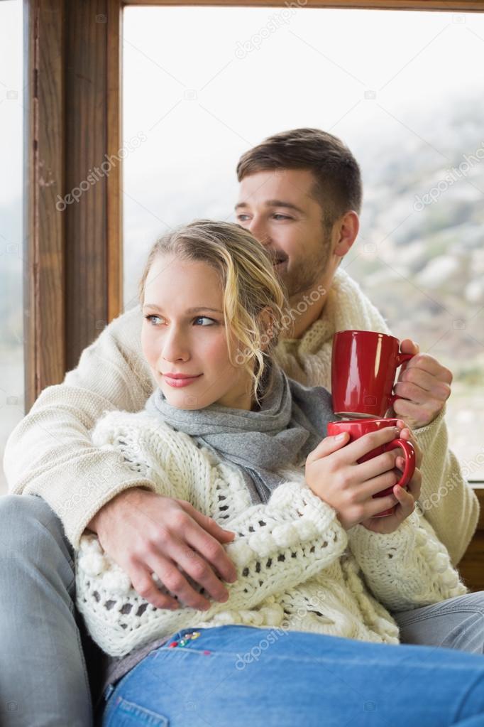 Couple in winter wear with cups looking out through window