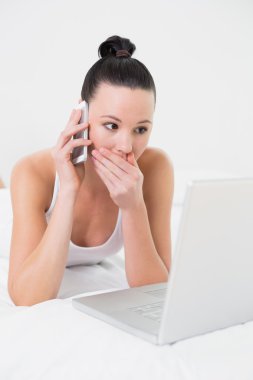 şok kadın yatakta kullanarak cep telefonu ve laptop