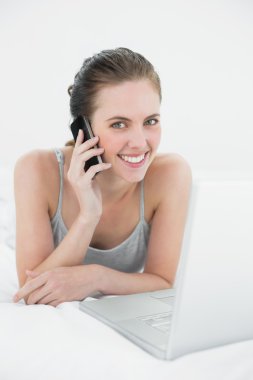 gülümseyen casual kadın yatakta kullanarak cep telefonu ve laptop