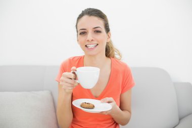 neşeyle kameraya gülümseyen bir bardak tutan çekici esmer kadın