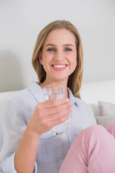 Szczęśliwy dzień blondynka siedzi na kanapie, trzymając szklankę wody — Zdjęcie stockowe