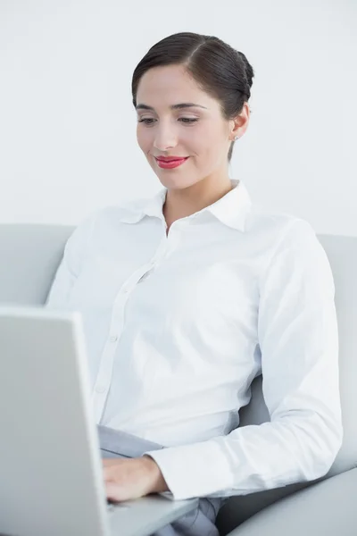 Χαμογελώντας καλά ντυμένος γυναίκα, χρησιμοποιώντας φορητό υπολογιστή στον καναπέ — Φωτογραφία Αρχείου