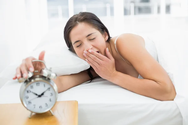 Mujer bostezando mientras extanding mano a reloj despertador — Foto de Stock