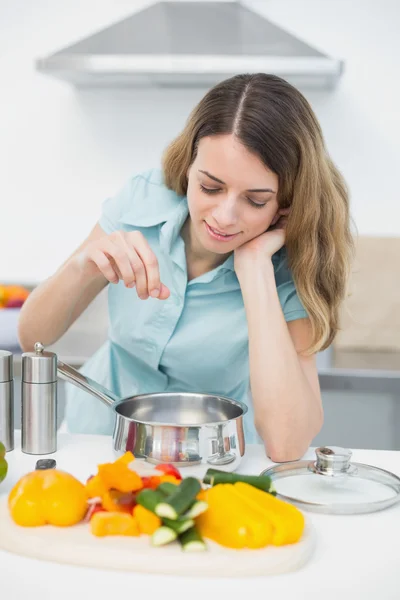 Conteúdo mulher morena cozinhar com legumes de pé na cozinha — Fotografia de Stock