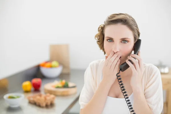 Chockad söt kvinna ringer i hennes kök med en telefon — Stockfoto