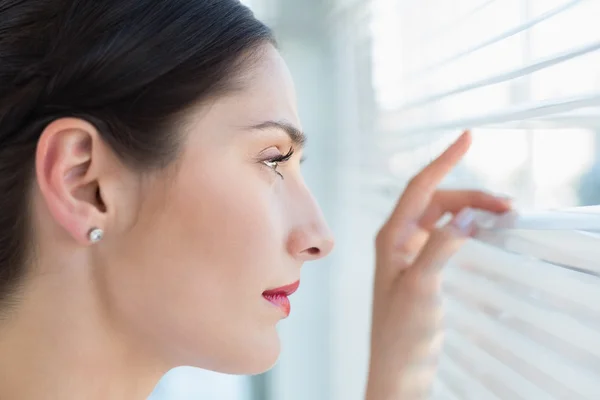 Young business woman peeking through blinds at office — Stock Photo, Image