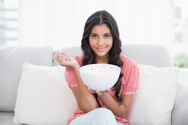 Zawartość ładny brunetka siedzi na kanapie, trzymając popcorn miski — Zdjęcie stockowe