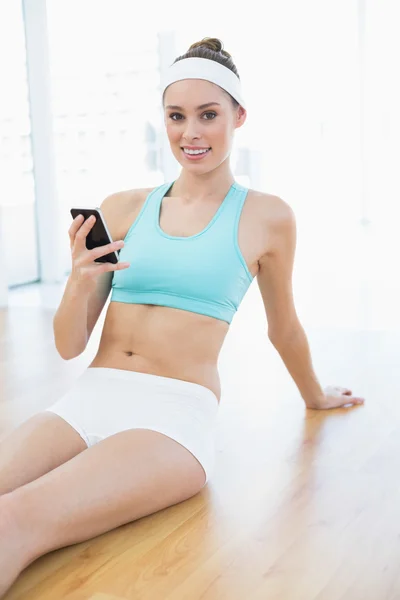 Conteúdo sorridente mulher segurando seu smartphone sentado no chão — Fotografia de Stock